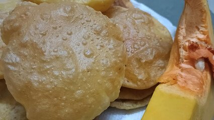 Golden fried pumpkin poori served hot with a raw slice of pumpkin on the side, showcasing traditional Indian festive or breakfast dish.