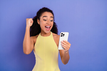 Excited woman holding a smartphone and celebrating a joyful moment against a vibrant purple...