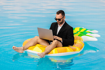 Young freelance businessman having a video call on a laptop while sitting on an inflatable in a...