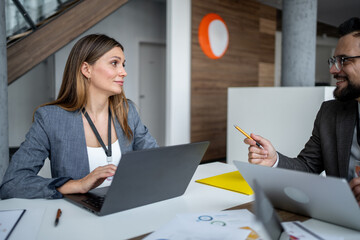 Businesspeople working together on laptops in modern office discussing charts and statistics