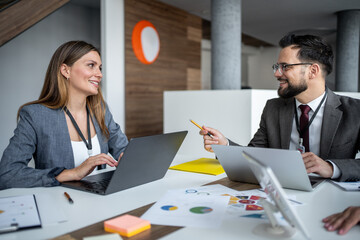 Business colleagues discussing using laptops in modern office