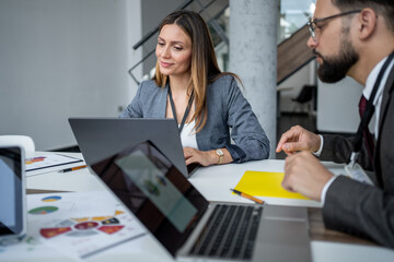 Businesswoman working on laptop with male colleague discussing charts in modern office