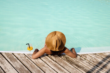 Beautiful woman in a hat enjoying relaxation in the pool with a cocktail. Concept leisure, summer...