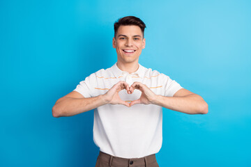 Young man creating a heart gesture with hands on blue backdrop symbolizing love, happiness, and...