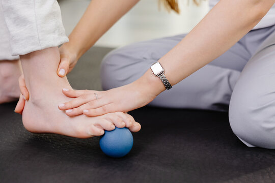 Physiotherapist helping patient exercising foot with small ball