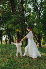 Happy young mother playing with her baby on the grass in a sunny park. Family bonding, early...