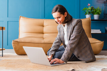 Beautiful woman sitting on the floor in the office and working on her laptop.