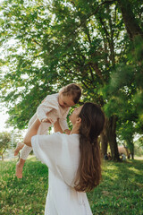 Happy young mother playing with her baby on the grass in a sunny park. Family bonding, early...
