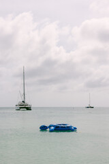 Relaxing on blue float in serene ocean with sailboats in the distance on a cloudy day
