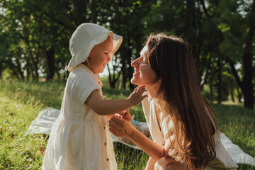Happy young mother playing with her baby on the grass in a sunny park. Family bonding, early...