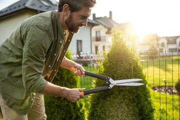 Young caucasian man cutting bushes with a prune in the garden