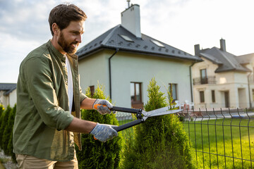 Young caucasian man cutting bushes with a prune in the garden