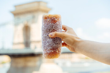 Hand Holding Kürtőskalács in Front of Chain Bridge