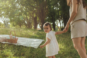 Happy young mother playing with her baby on the grass in a sunny park. Family bonding, early...