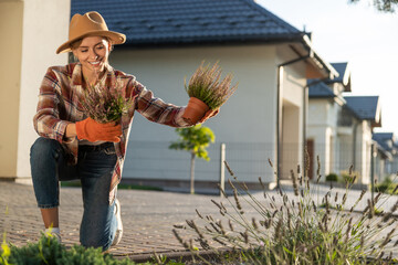 Cute young woman in straw hat planting the flowers in her garden
