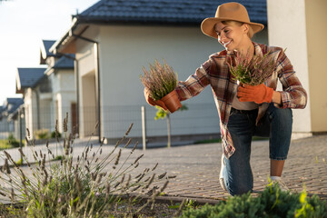 Cute young woman in straw hat planting the flowers in her garden