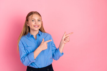 Young girl in blue shirt pointing with fingers against pink background with happy expression