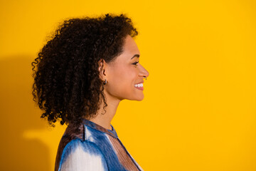 Profile view of a young confident woman with curly hair against a vibrant yellow backdrop,...