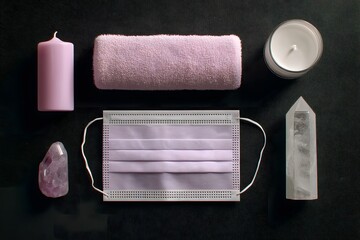 Obraz premium Soft pink towel, candle, crystal, and face mask arranged artistically on a dark background, creating a serene atmosphere for wellness and relaxation concepts