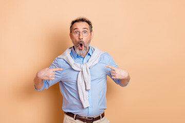 Portrait of a mature businessman expressing surprise and pointing, standing against a beige...