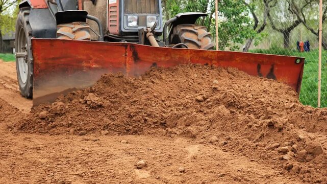 Tractor leveling ground with dozer blade on a sunny day