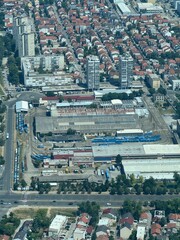 An aerial view captures a sprawling tram depot amidst urban development, with numerous trams visible on tracks and surrounded by residential buildings and streets under a clear sky.