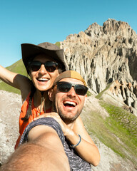 Cheerful couple of hikers friends taking selfie on top of mountain. Millennial guy girl enjoying summertime day out trip laughing at camera together - Millennial travelers standing in scenic nature