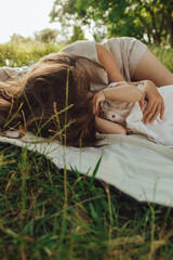 Happy young mother playing with her baby on the grass in a sunny park. Family bonding, early...