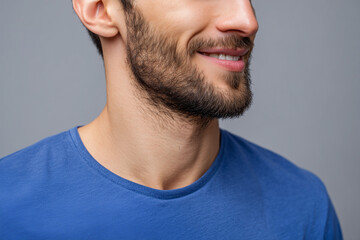 Fototapeta premium Close-up of a smiling young man with a beard wearing a blue t-shirt against a gray background