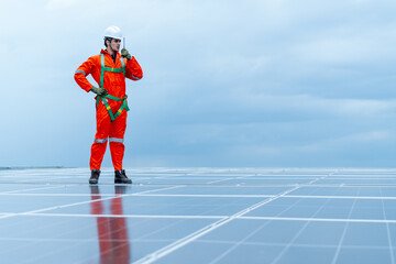 Technician or factory worker use walkie talkie to contact co-worker during maintenance rooftop solar cell system with cloudy sky.