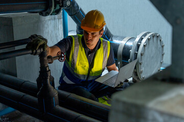 Factory worker man use laptop to check pipe system under part of factory building.