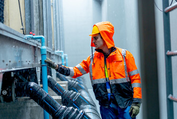 Close up factory worker or technician with raincoat check and maintenance pipe system in area of factory building during raining.