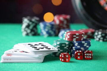 Casino chips, dice and playing cards on green table against blurred lights, closeup