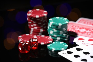 Casino chips, playing cards and dice on mirror surface against blurred lights, closeup