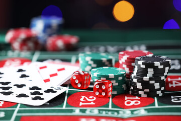 Casino chips, dice and playing cards on roulette table against blurred lights, closeup