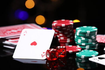 Casino chips, playing cards and dice on mirror surface against blurred lights, closeup