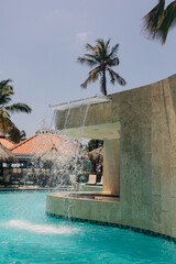 Tranquil swimming pool with cascading waterfall and palm trees on a sunny day in a tropical resort