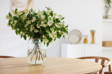 Bouquet of beautiful jasmine flowers in vase on wooden table indoors. Space for text