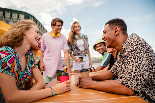 Young diverse friends enjoying coffee outdoors on a sunny day while socializing in a vibrant urban setting - Powered by Adobe