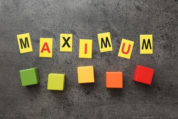 Word Maximum and colorful cubes on grey table, flat lay