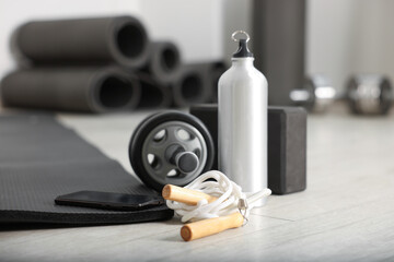 Phone and different fitness equipment on floor in gym, closeup