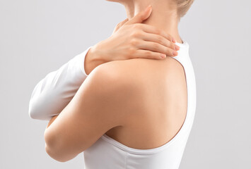 Slender woman in white bodysuit on isolated background. She gives herself shoulder and neck...