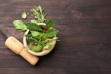 Mortar with different fresh herbs, peppercorns and pestle on wooden table, flat lay. Space for text