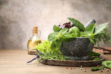 Mortar with different fresh herbs and peppercorns on wooden table against grey background, closeup