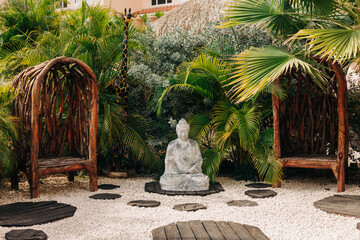 Serene garden setting featuring a Buddha statue surrounded by lush greenery and unique wooden...