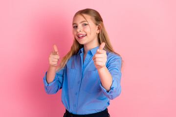Young blonde girl smiling and pointing with her fingers, wearing a blue shirt in front of a pink...