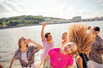 Joyful group of friends dancing by the waterfront on a sunny day, enjoying summer vibes and time...