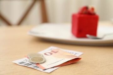 Tips and receipt on wooden table in restaurant, closeup. Gratuity for work