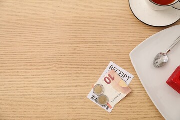 Tips, receipt and dishware on wooden table, flat lay. Space for text