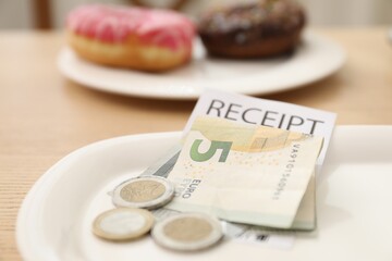 Tips and receipt on wooden table in restaurant, closeup. Gratuity for work